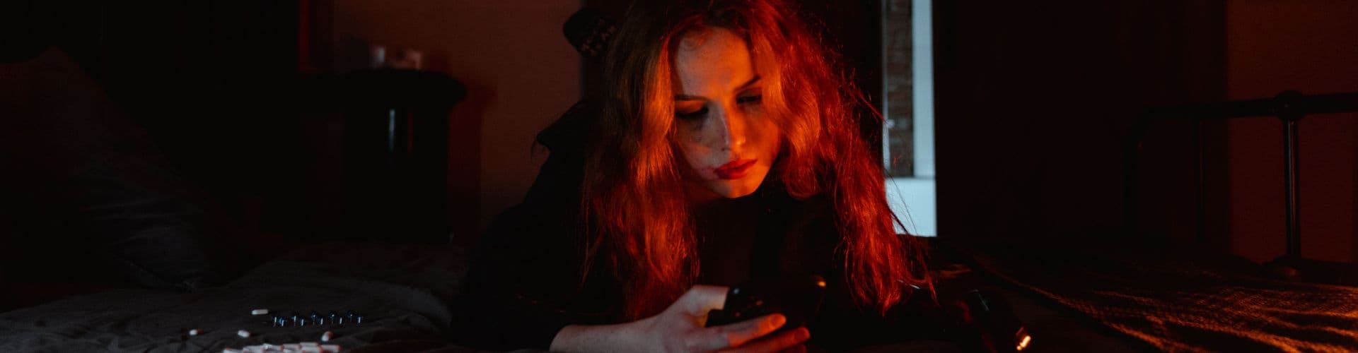 Mulher deitada olhando o celular à noite, luz vermelha