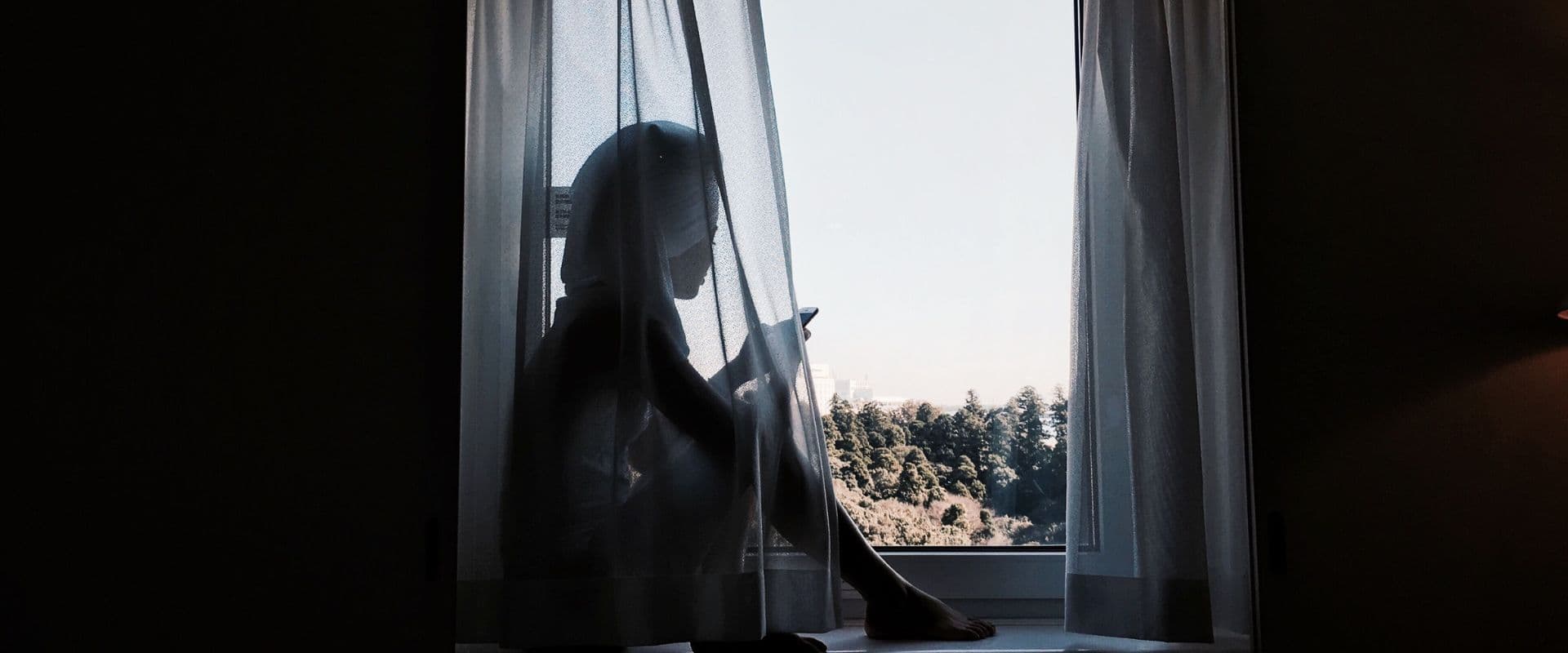 Silhueta feminina olhando pela janela ao entardecer