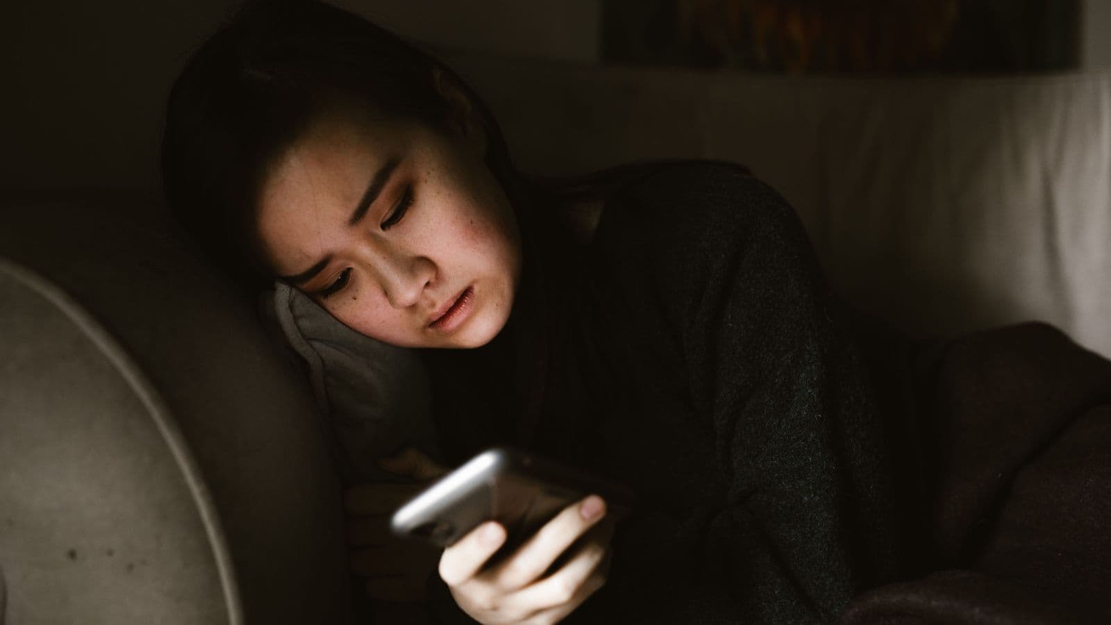 Mulher olhando o celular à noite, tela iluminando o rosto